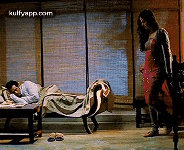 a woman is standing in front of a man sleeping on a bed .