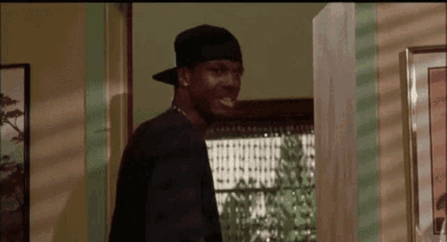 a man wearing a baseball cap and a black shirt is standing in a living room .