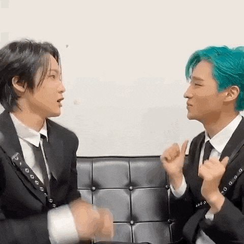 two men in suits are sitting next to each other on a couch and talking to each other .
