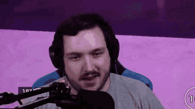 a man wearing headphones and a microphone is sitting in front of a purple wall .