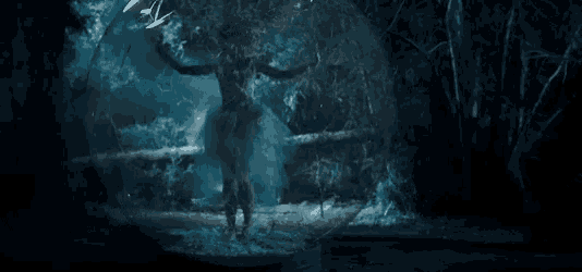 a person is standing in a dark forest with a sword in their hand .
