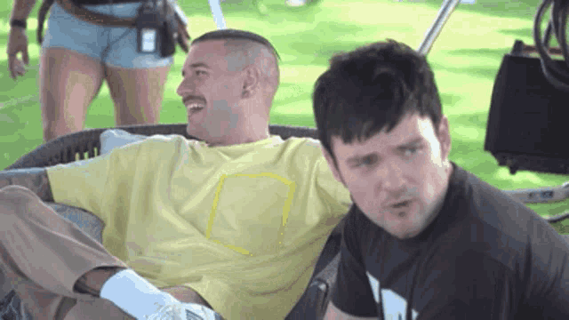 a man in a yellow shirt is sitting next to another man in a black shirt with the letter w on it