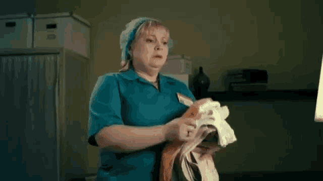a woman in a blue scrub top is holding a bunch of clothes in her hands .