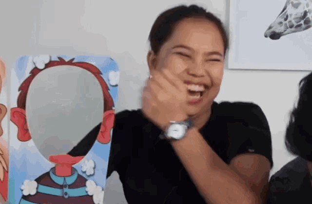a woman wearing a watch is laughing in front of a cardboard cutout of her face .