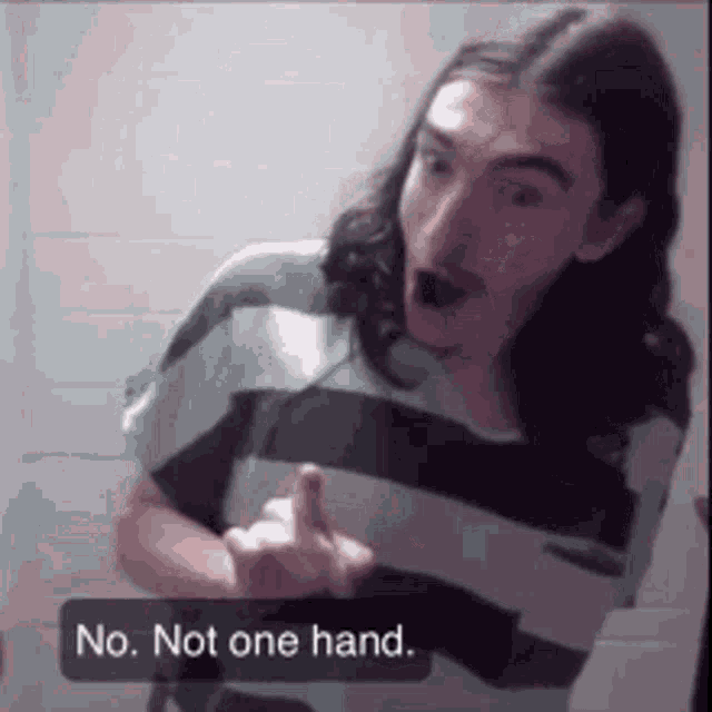 a man with long hair and a mustache is making a funny face and giving the middle finger .