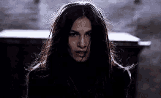a woman with long dark hair is standing in front of a trash can .