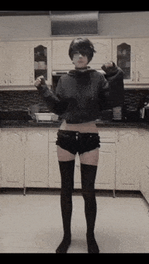 a girl in a hoodie and shorts stands in a kitchen