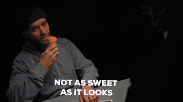 a man sitting at a table eating an ice cream cone with the words not as sweet as it looks above him .