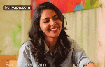 a woman is smiling while sitting at a table in front of a wall .