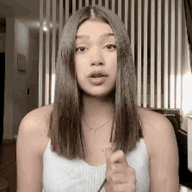 a woman in a white tank top is pointing her finger at the camera .