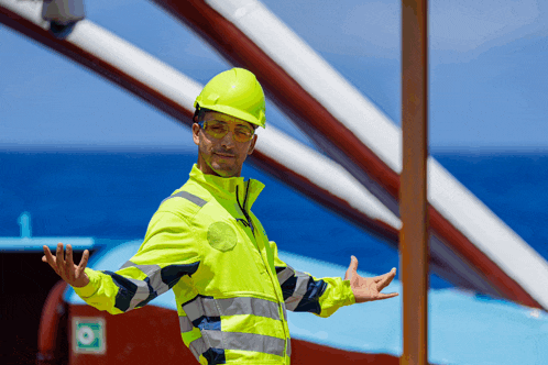 a man wearing a yellow hard hat and safety vest is standing with his arms outstretched