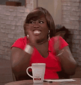 a woman in a red shirt is sitting at a table with a mug that says the talk