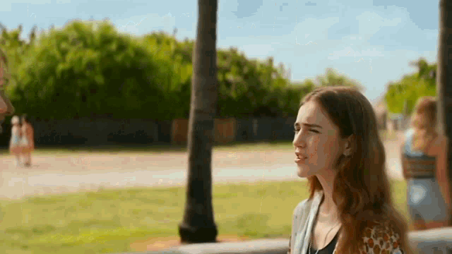 a woman with long red hair is standing in a park with a palm tree in the background .