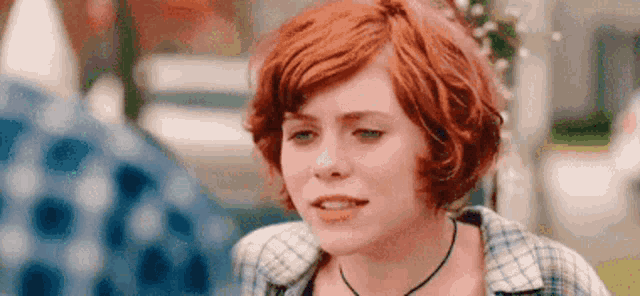 a close up of a woman with red hair wearing a plaid shirt and a choker .