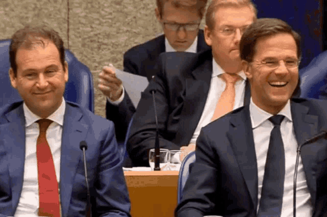 two men in suits and ties are laughing in a room
