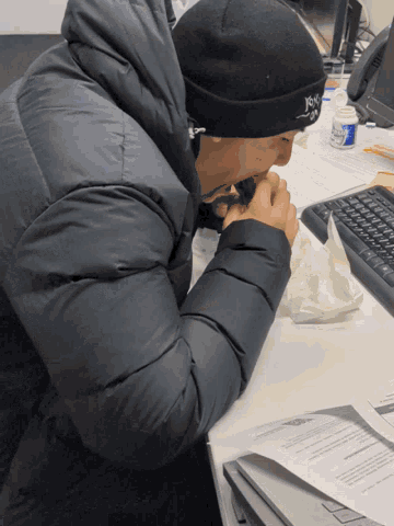 a man wearing a black hat that says ' just do it ' on it sits at a desk
