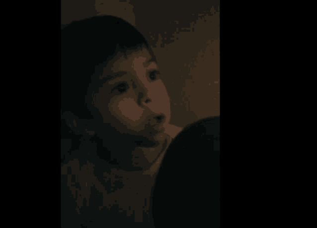a young boy in a white shirt looks at something in the dark