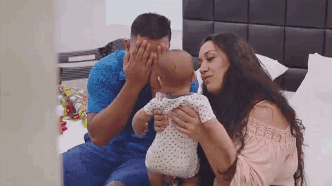 a man and woman are holding a baby on a bed .