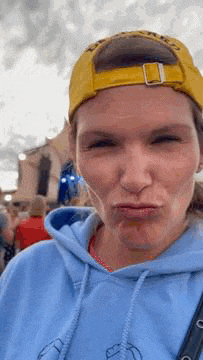 a woman wearing a blue hoodie and a yellow hat is making a face .