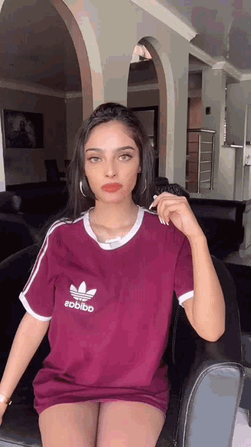 a woman wearing a maroon adidas shirt is sitting on a chair