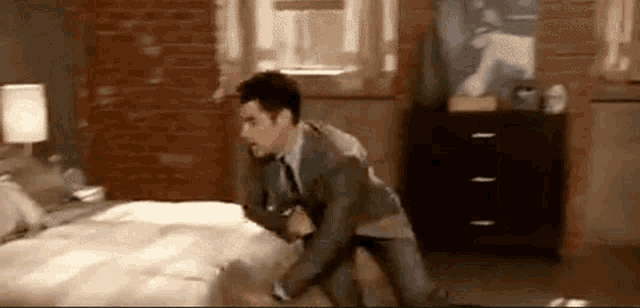 a man in a suit is standing next to a bed in a bedroom .