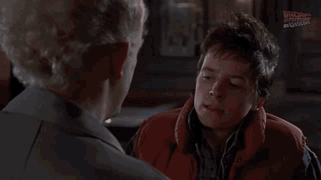 a man in a red vest talks to a man in a suit and the man in the suit says thanks