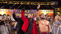 a group of wrestlers are standing in front of a crowd with their arms in the air .