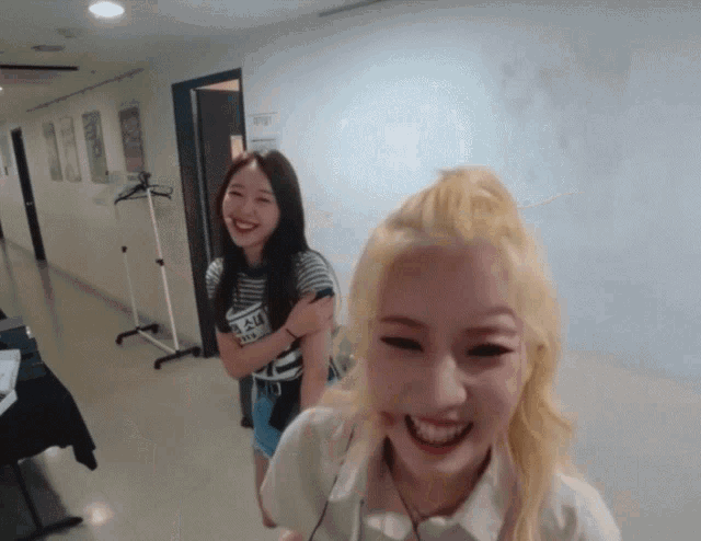 two girls are smiling in a hallway with one wearing a shirt that says ' nct ' on it