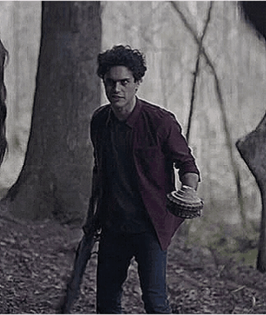 a man in a red shirt is standing in the woods holding a knife .