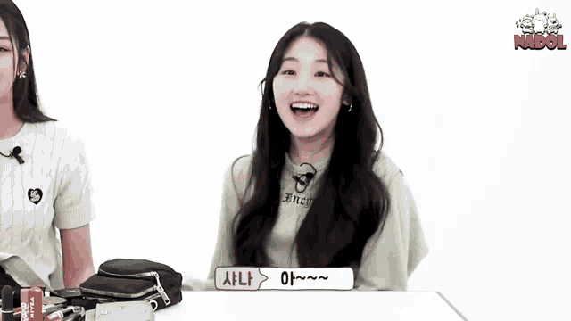 a girl is sitting at a table with her hands in the air and smiling at the camera .