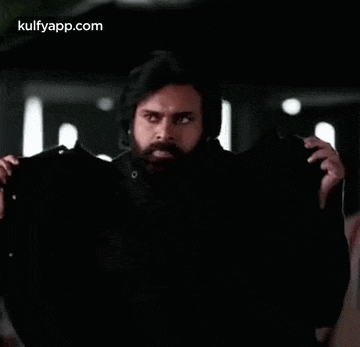 a man with a beard is wearing a black jacket and dancing in a dark room .