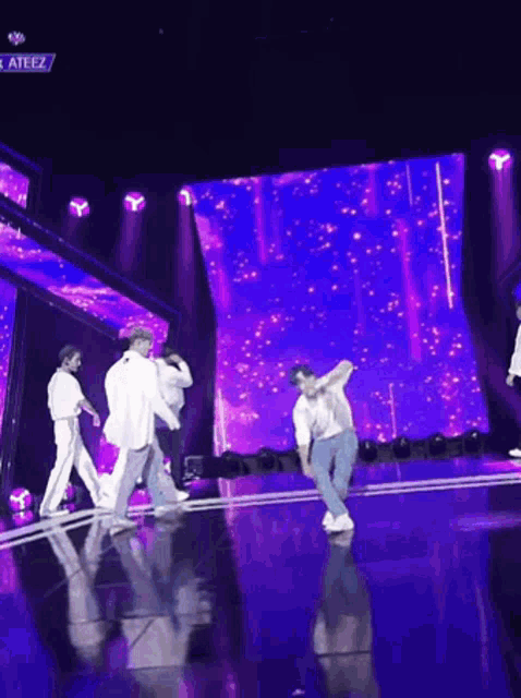 a group of people are dancing on a stage in front of a large purple screen .