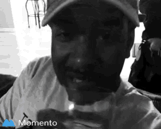 a black and white photo of a man wearing a hat and holding a can of soda .