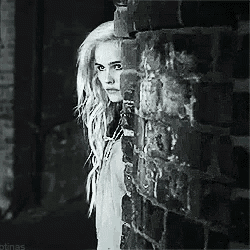a woman is peeking over a brick wall .