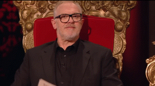 a man wearing glasses and a black suit is sitting in a red chair