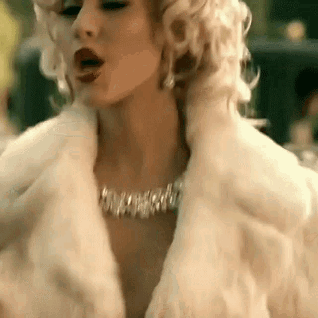 a woman wearing a white fur coat and a necklace is standing in front of a car .
