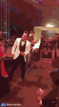 a man in a tuxedo is dancing on a stage while a man playing a guitar stands behind him .