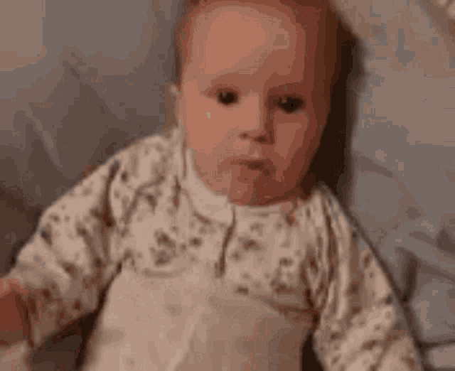a baby is sitting on a bed and making a face .