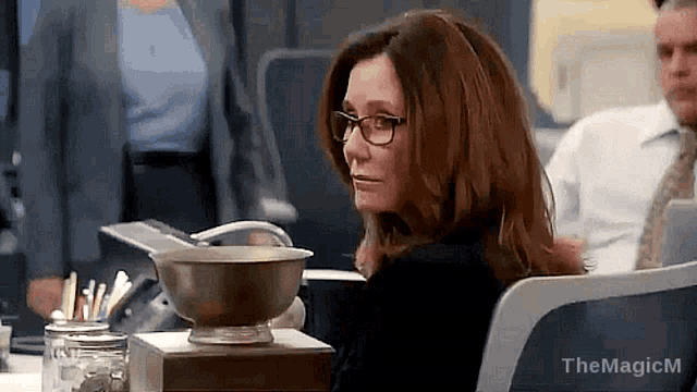 a woman wearing glasses is sitting at a desk in an office .