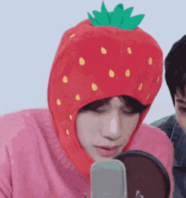 a man wearing a pink sweater and a strawberry hat is looking at himself in a mirror .