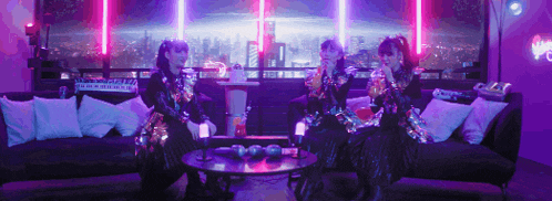 three women are sitting on a couch in a room with purple lights behind them