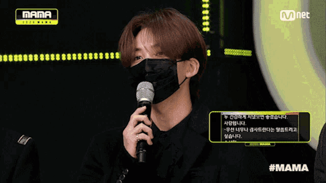 a man wearing a mask is holding a microphone in front of a mama logo