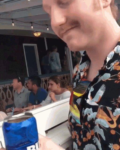 a man in a floral shirt is holding a blue can that says ' ri ' on it