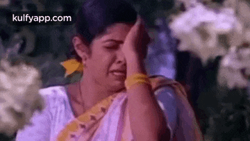a woman is covering her face with her hand while crying in front of flowers .