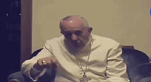 a man in a white robe is sitting in a chair with a cross on his neck .