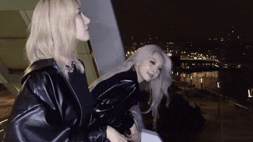 two blonde women are standing next to each other in front of a window
