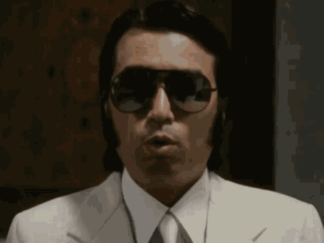 a man wearing sunglasses and a white suit has his mouth open