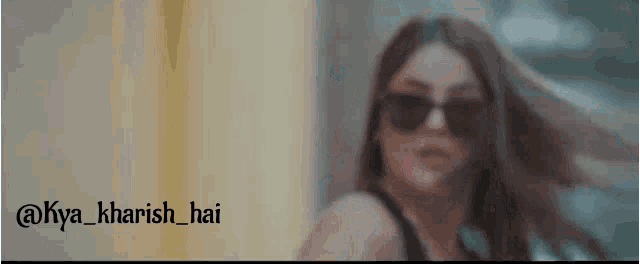a woman wearing sunglasses is standing in front of a wall .