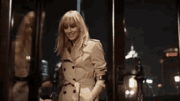 a woman wearing a trench coat is standing in front of a window .