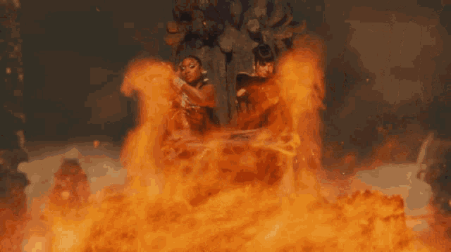 two women are surrounded by flames in a dark scene